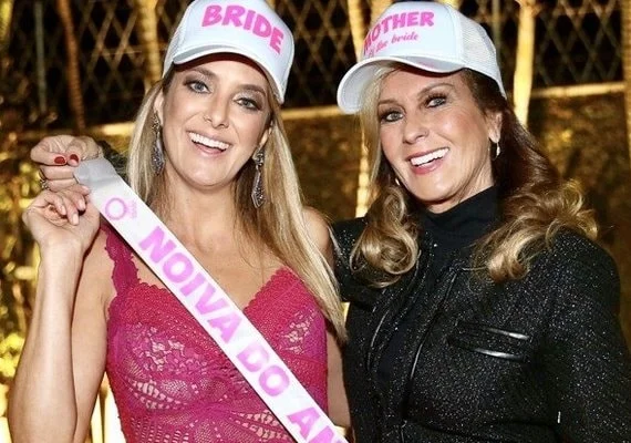 Foto da apresentadora Ticiane Pinheiro segurando faixa com dizeres: a noiva do ano, com a mãe Helô Pinheiro ao lado